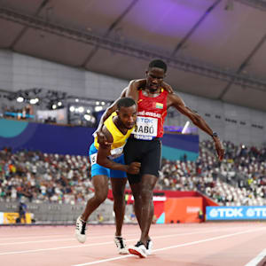 Braima Suncar Dabo helps Jonathan Busby in the home straight in their 5000m heat in Doha