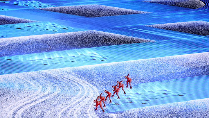 Конькобежцы расчищают снег, чтобы показать олимпийский девиз 